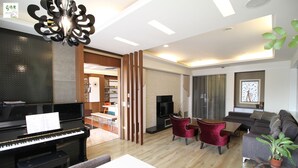 A modern living room with a piano, red chairs, a grey sofa, and a fireplace.