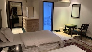Ein Hotelzimmer mit zwei Betten, einem kleinen Schreibtisch, einem Sessel, einem Balkon mit Blick und einer Klimaanlage.