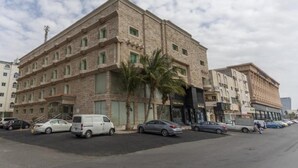Ein mehrstöckiges Hotel mit einer Stein-Fassade, mehreren parkenden Autos und Palmen davor.