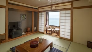 A traditional Japanese room with tatami flooring, a television, a table with a decorative bowl, and a view of the sea through shoji screens. - The Hotel Yakushima (Yakushima)