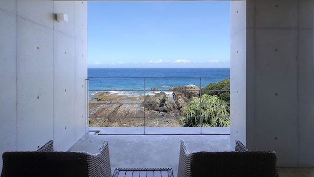 A balcony with wicker furniture and a view of the ocean and rocky coastline. - The Hotel Yakushima (Yakushima)