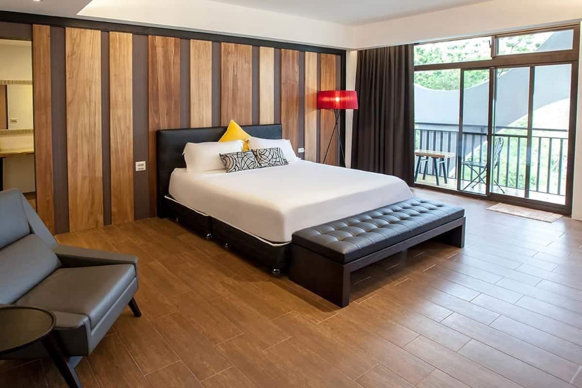 A modern hotel room with a large bed, a bench, a chair, and a view of the outdoors.