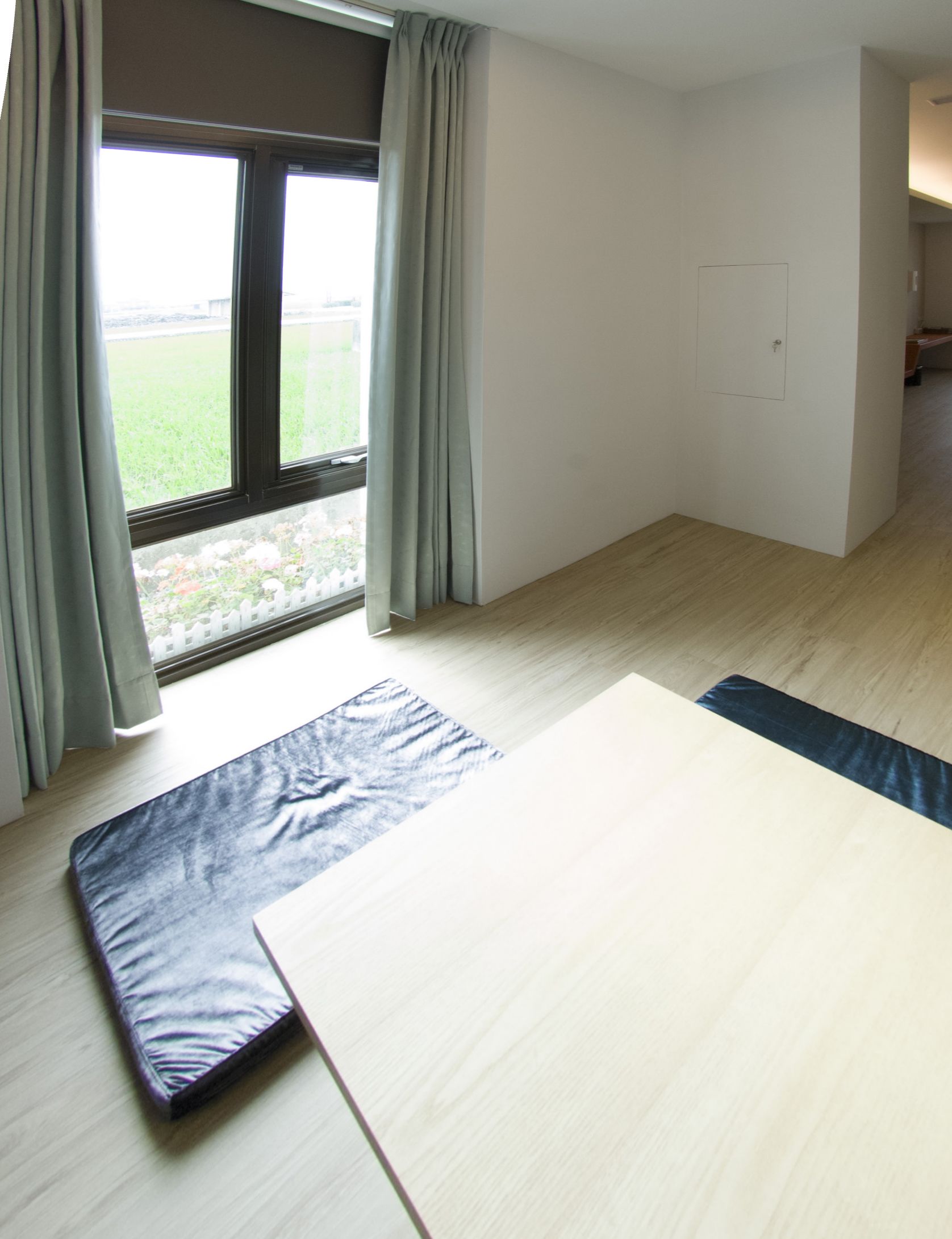 Una habitación con un ventanal grande, suelo de madera clara y una cama con edredón de estampado azul y blanco.