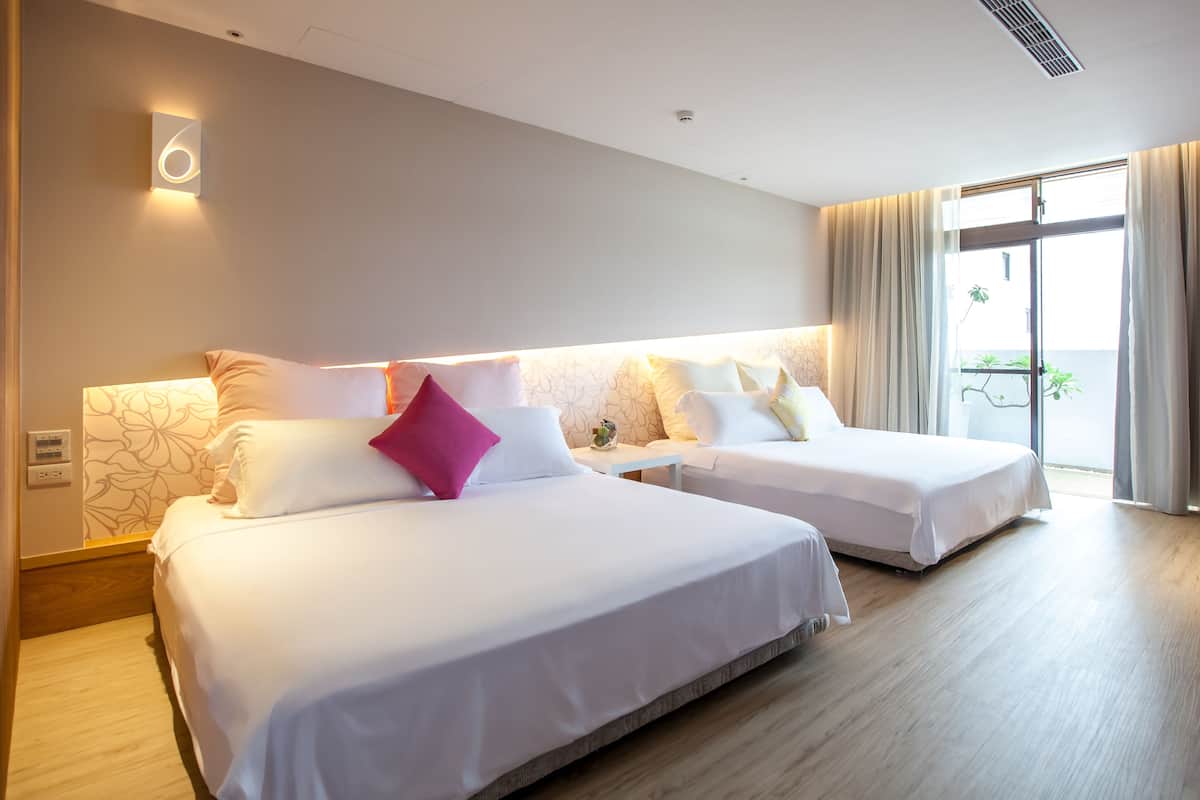 A hotel room with two beds, a small table, and a view of the outdoors.