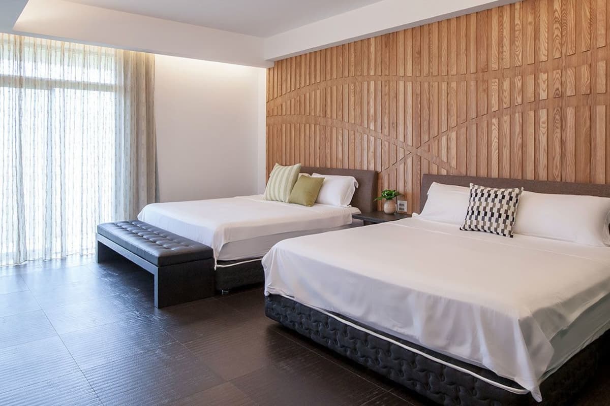 A modern hotel room with two beds, a wooden accent wall, and a large window with sheer curtains.