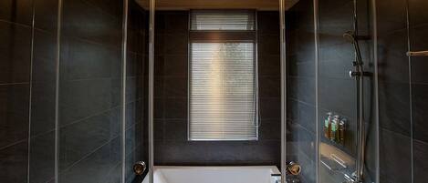 A modern bathroom with a glass-enclosed shower, a large window, and a bathtub.