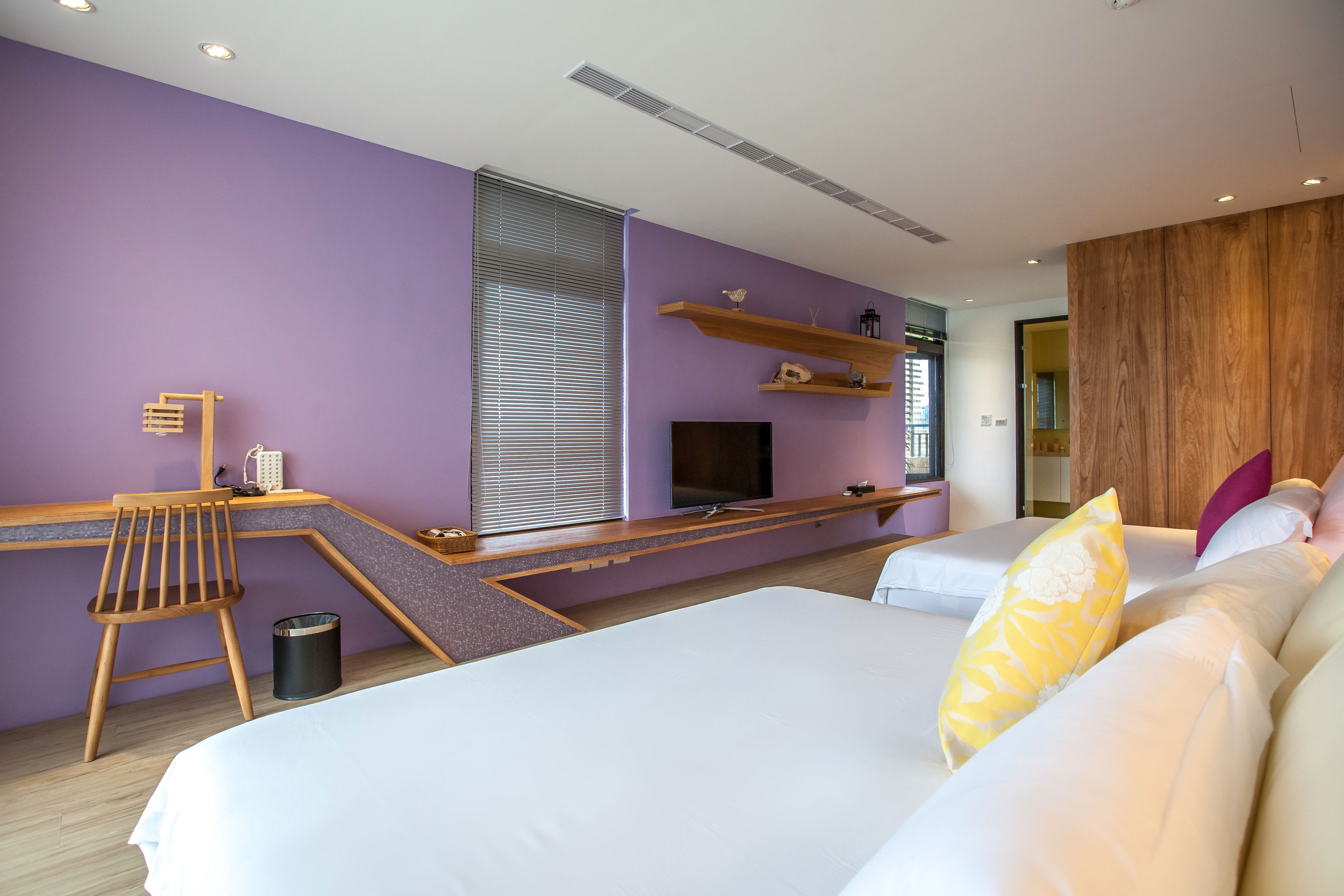 A modern hotel room with a large bed, a desk with a chair, a TV, and a wooden accent wall.