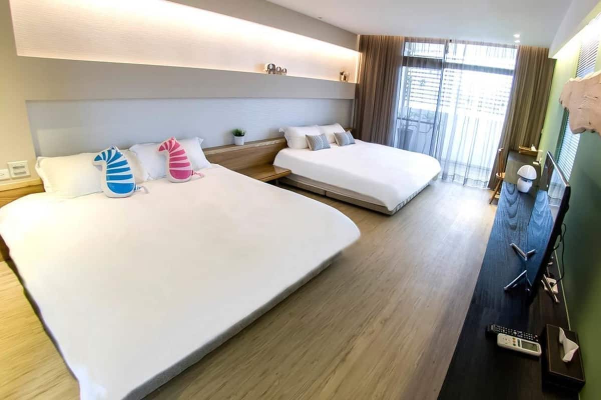 A hotel room with two beds, a desk, a chair, a TV, and a window with curtains.