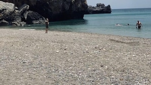 A rocky beach with clear water and a large rock formation in the background.