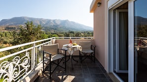 A balcony with a table and chairs, a view of mountains, and a glass door.