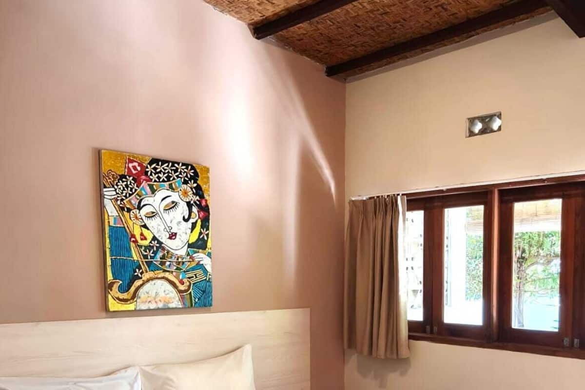 A bedroom with a bed, a painting, a window with curtains, and a ceiling with wooden beams.
