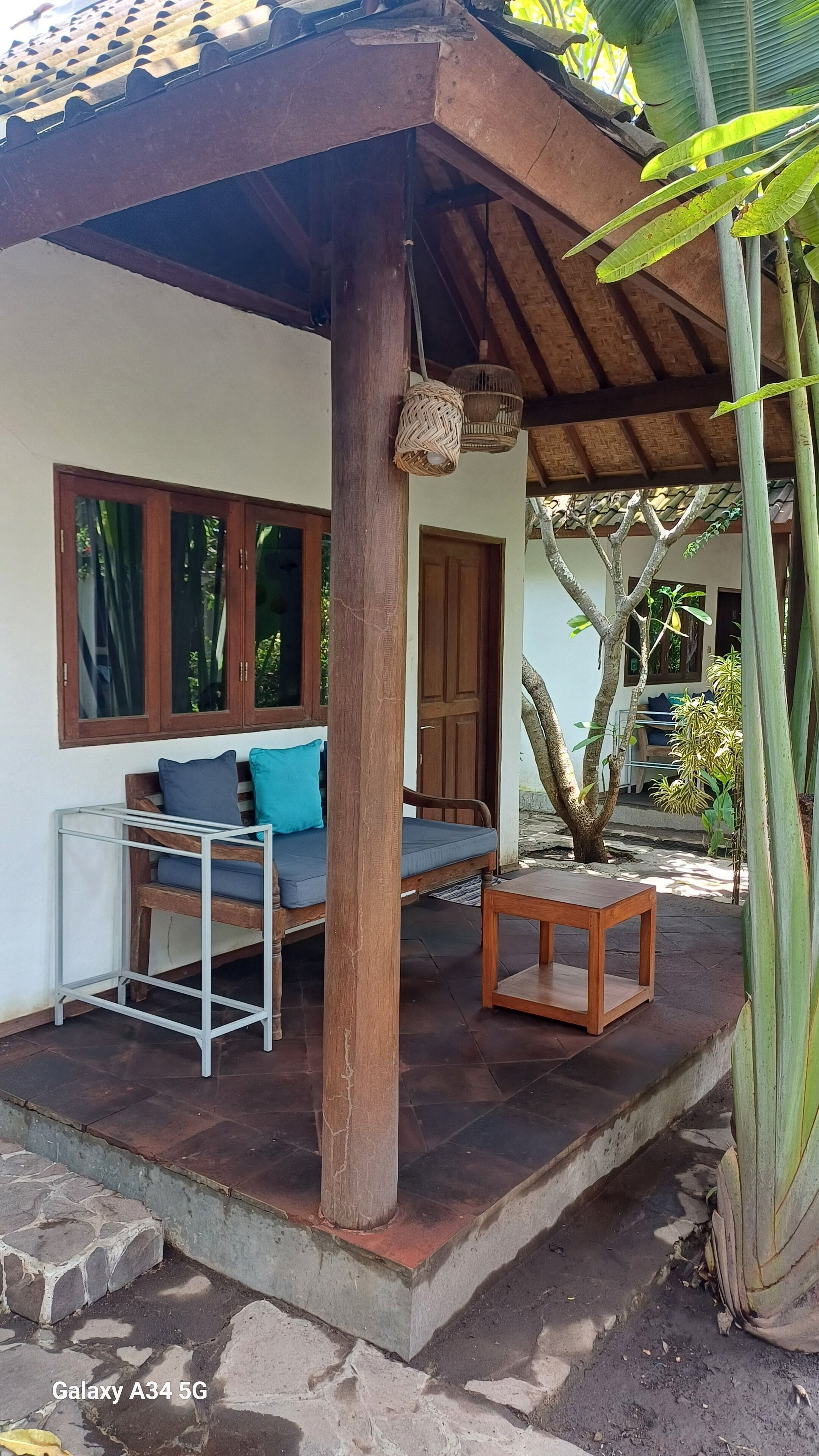 A covered outdoor seating area with a sofa and table, a wooden door, and a large plant.