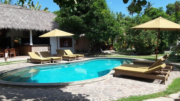 A swimming pool with lounge chairs and umbrellas, surrounded by a stone patio and lush greenery. - Si Pitung Village (Gili Air)