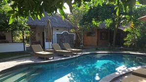 A swimming pool with lounge chairs and a thatched-roof building in the background. - Si Pitung Village (Gili Air)