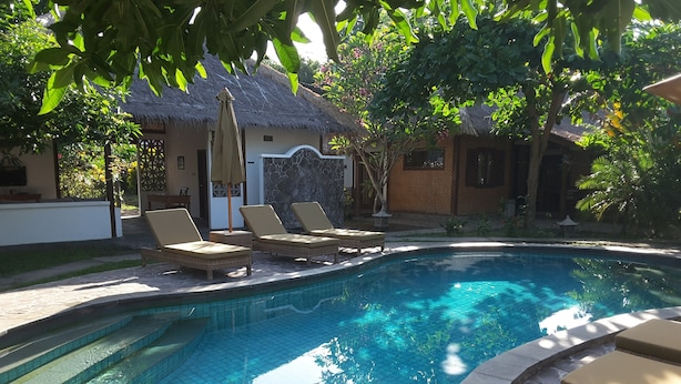 A swimming pool with lounge chairs and a thatched-roof building in the background. - Si Pitung Village (Gili Air)