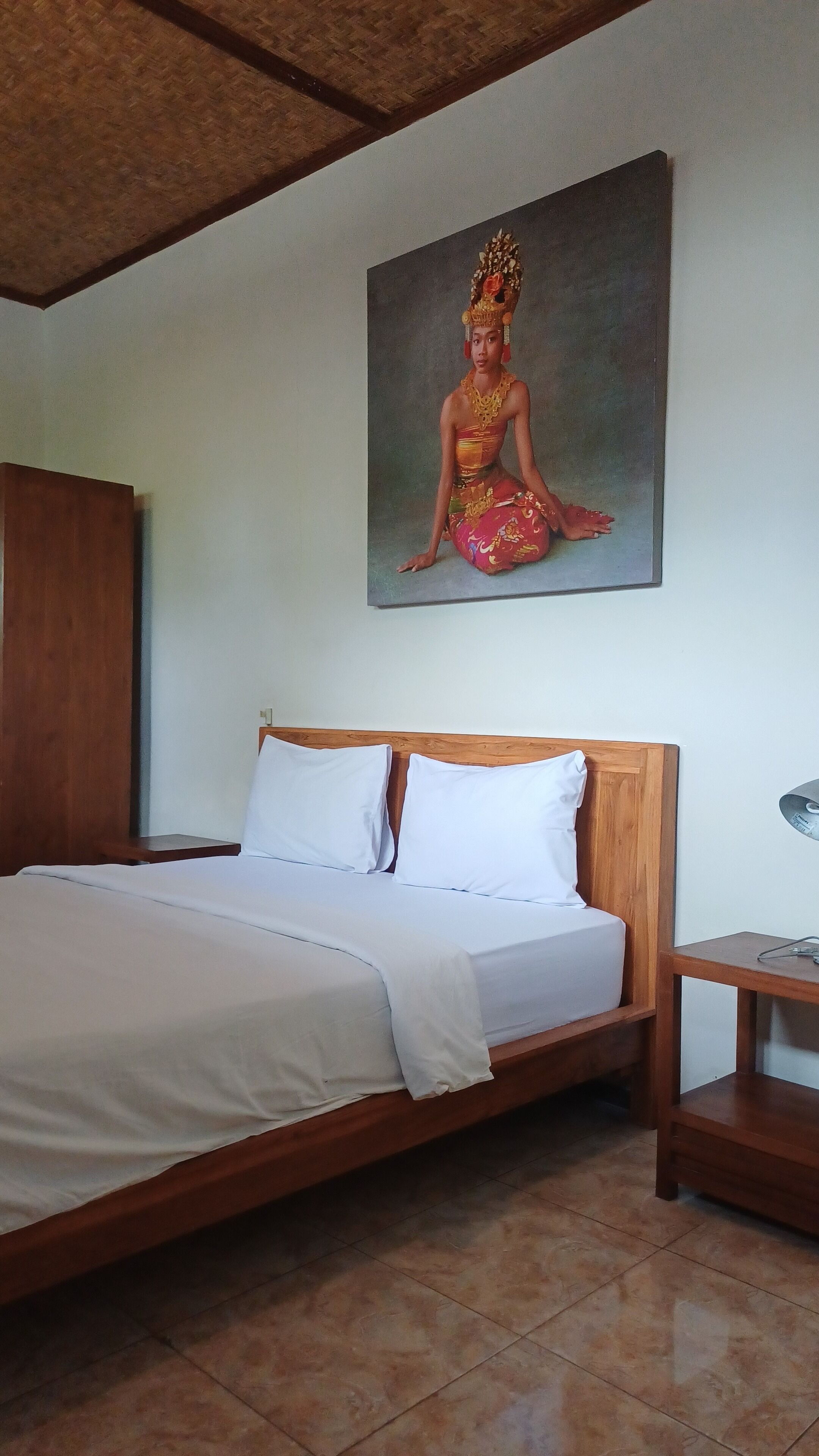 Un dormitorio con cama de madera, ropa de cama blanca, una mesita de noche y un cuadro de una persona vestida con traje tradicional en la pared.