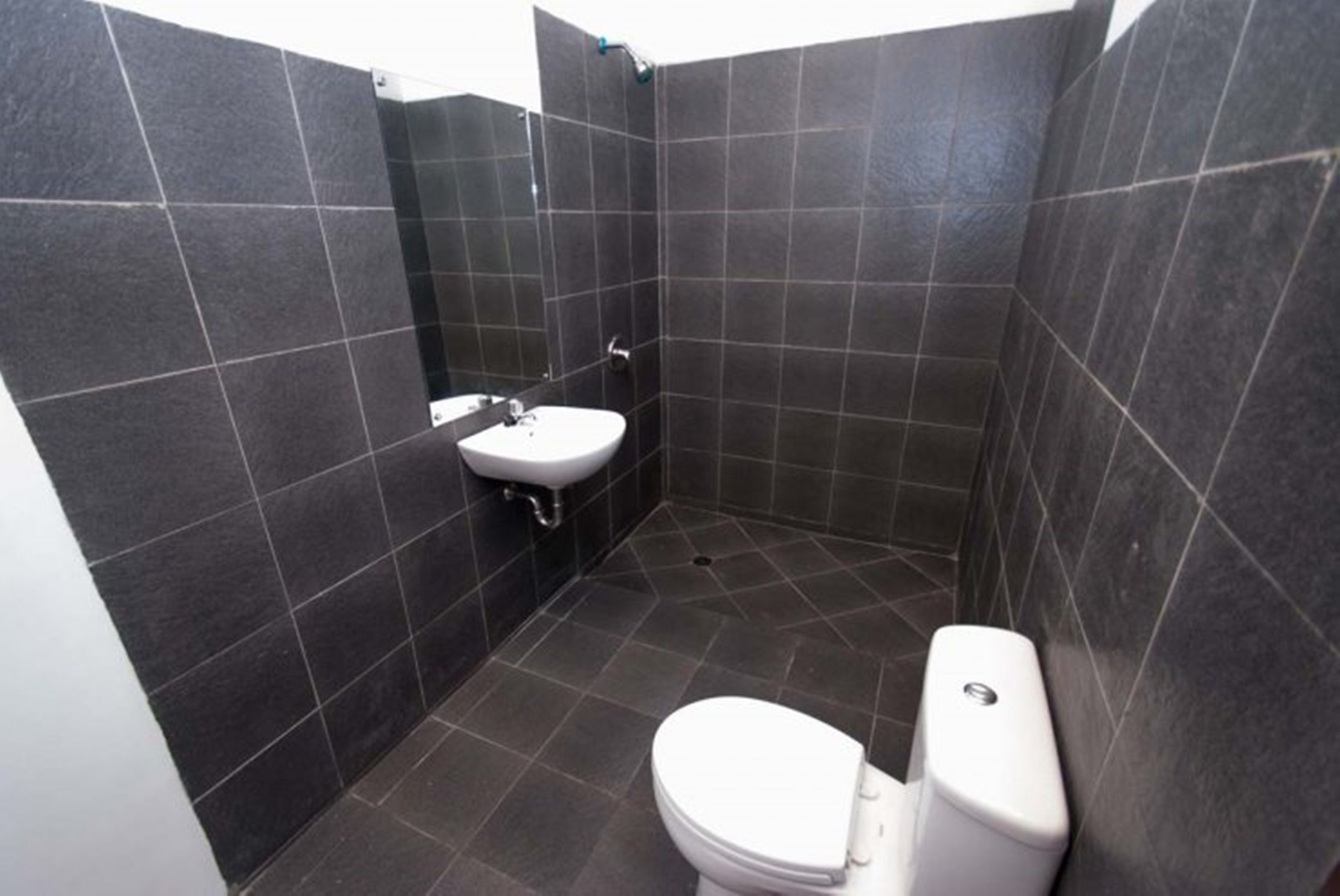 A small, dark-tiled bathroom with a white sink and toilet.