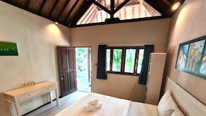 A bedroom with a large bed, a bedside table, a window with curtains, and a door leading outside. - Si Pitung Village (Gili Air)