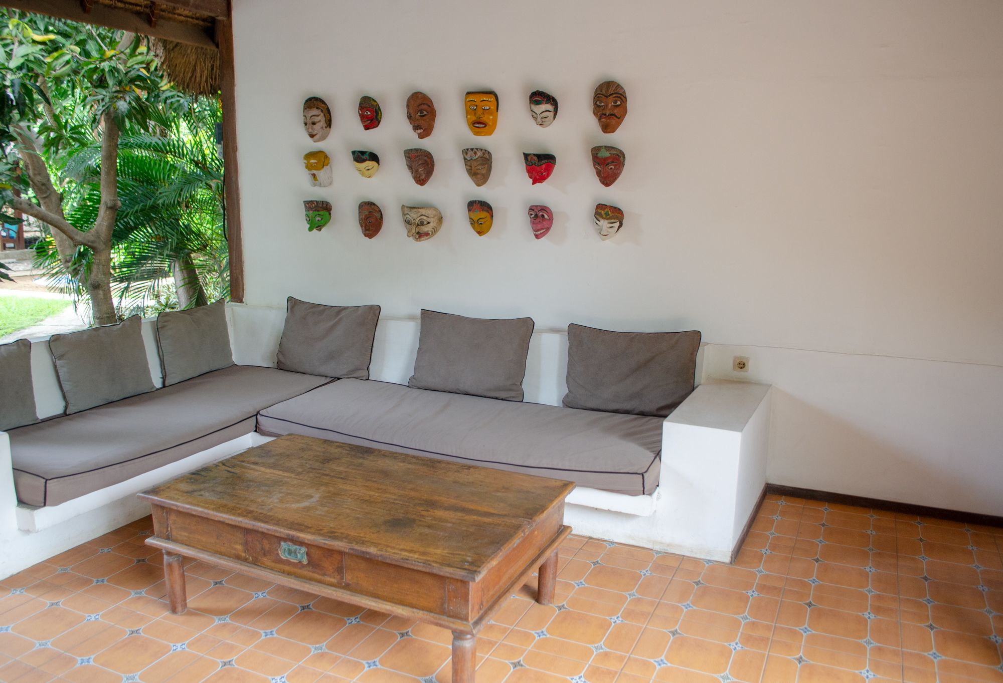 A modern living room with a sectional sofa, a wooden coffee table, and a wall decorated with various masks.