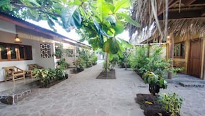 A courtyard with a thatched roof, stone flooring, and various plants. - Si Pitung Village (Gili Air)