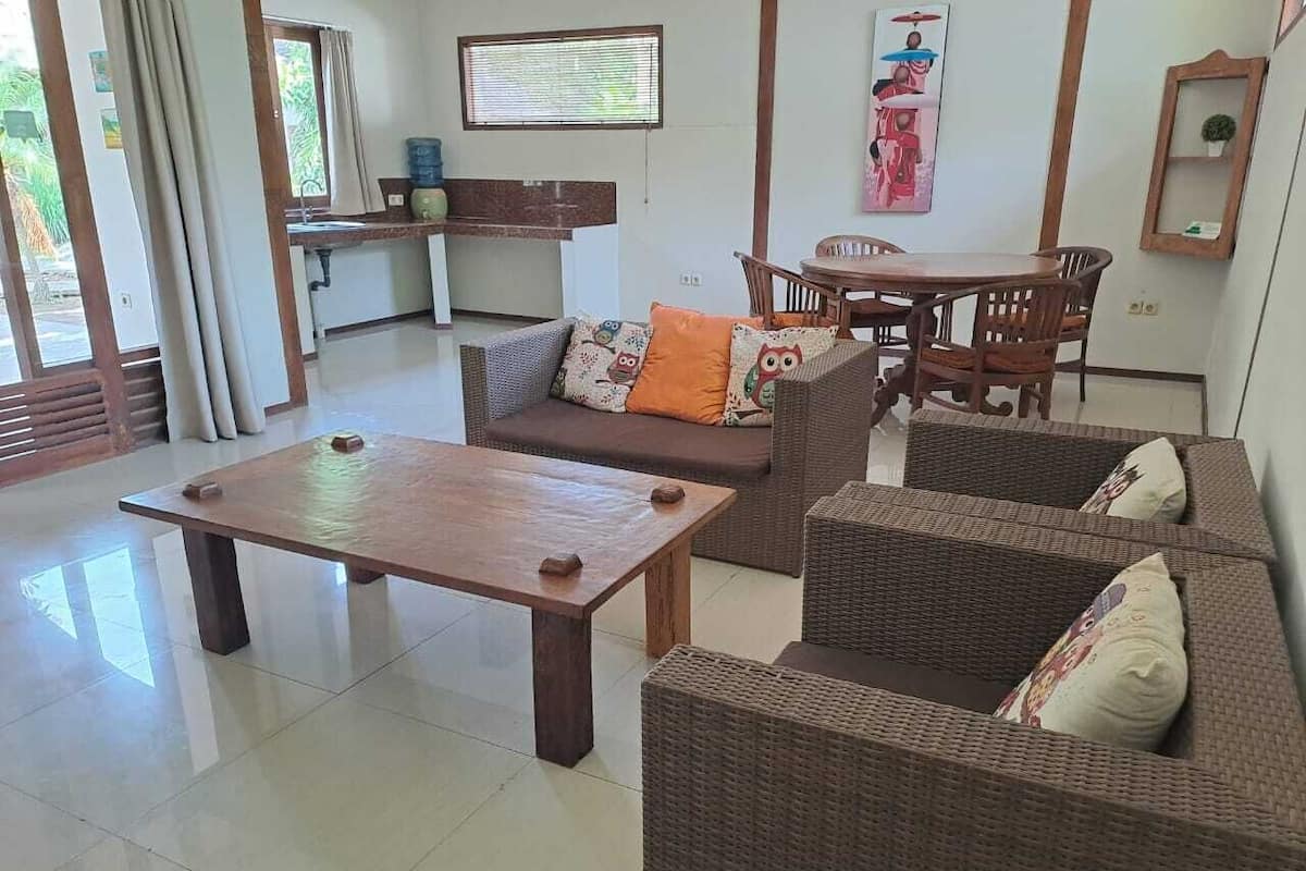 A living room with a wooden coffee table, wicker sofas, a dining table, and chairs.