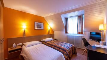 Une chambre d’hôtel avec deux lits, un bureau avec un ordinateur, une fenêtre avec des rideaux et des lampes fixées au mur.