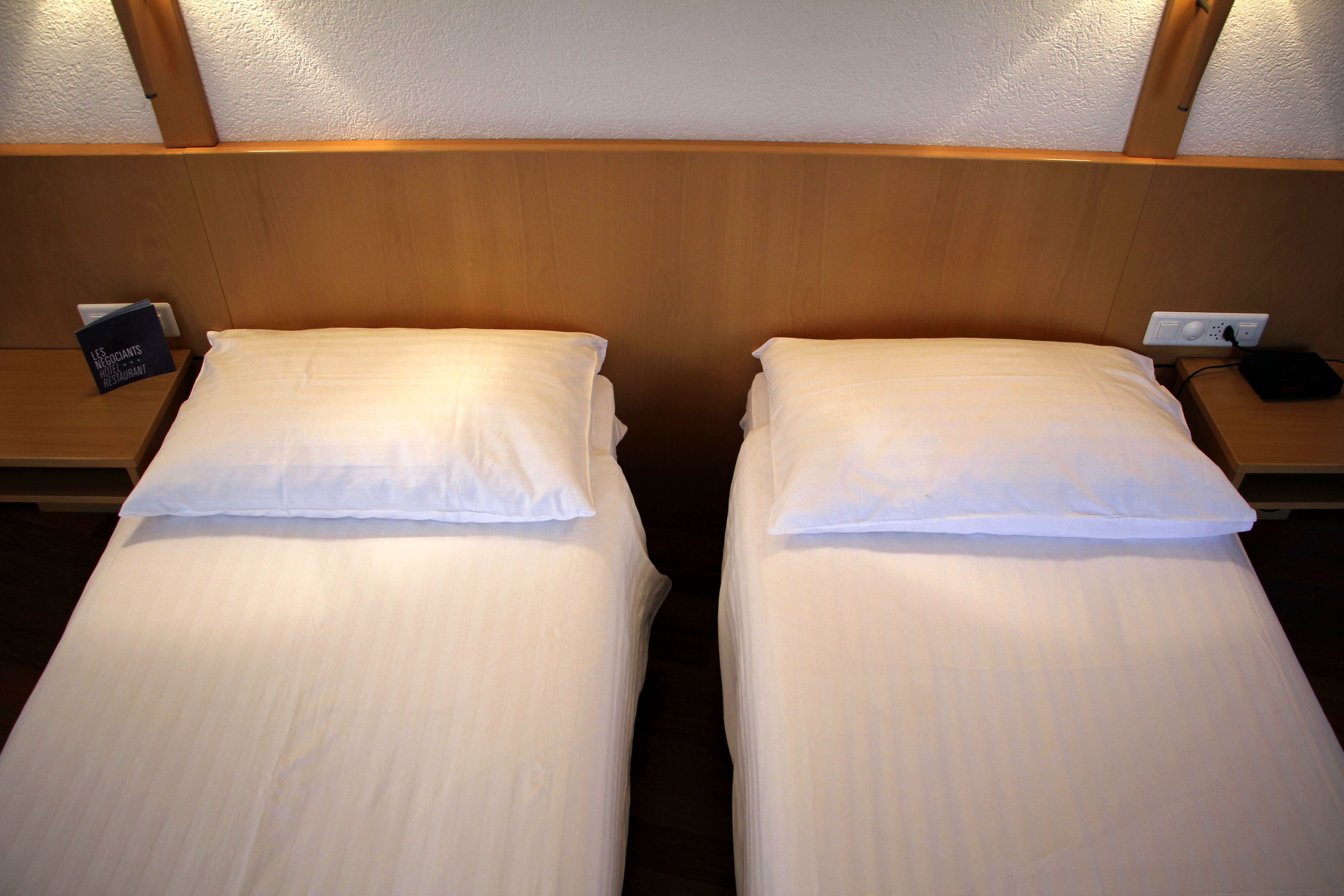 Cama doble con ropa blanca, cabecera de madera y mesita de noche con toma de corriente y teléfono.