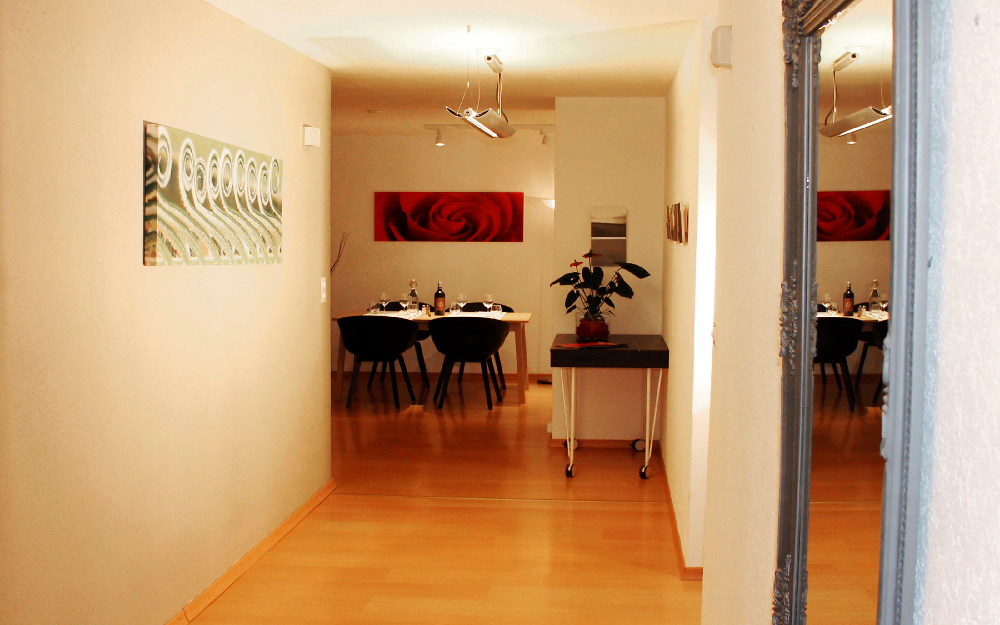 A dining area with a table set for four, a potted plant, and a red abstract painting on the wall.