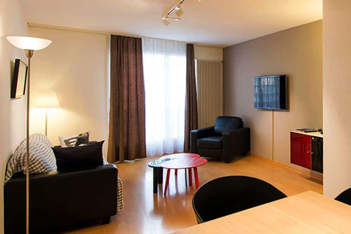 Ein kompakter Wohnbereich mit einer Couch, einem Esstisch und einem an der Wand montierten Fernseher.
