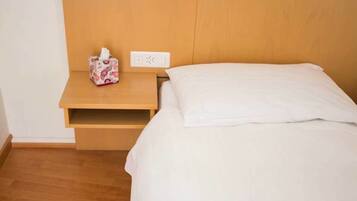 Habitación de hotel con cabecera de madera, mesita de noche y estuche de pañuelos, y cama blanca.