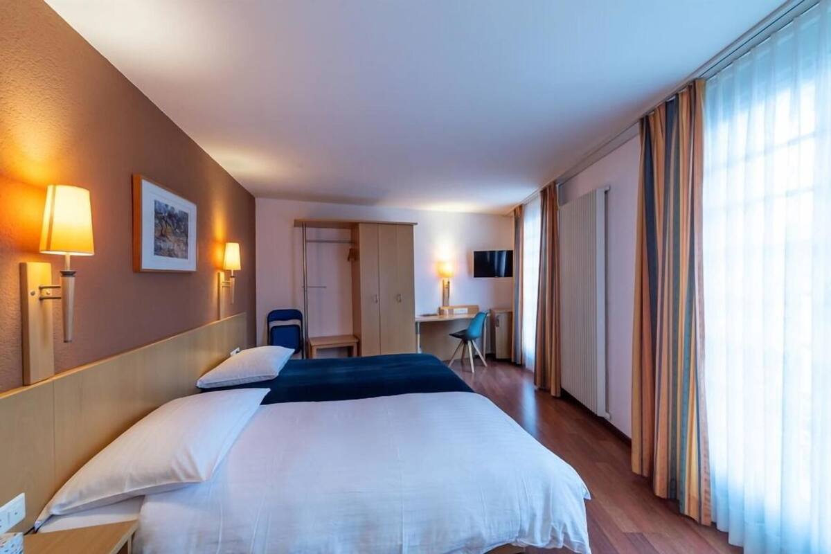 Ein Hotelzimmer mit Bett, Nachttischlampen, Schreibtisch, Stuhl und Fernseher.