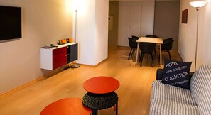 Ett kompakt hotellrum med ett litet kök, en matplats och en sittgrupp med en soffa och två små bord.