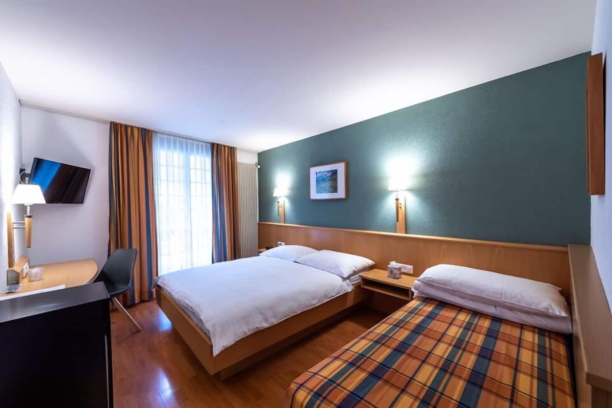 Ein Hotelzimmer mit Bett, Schreibtisch, Stuhl, Fernseher und einem Fenster mit Vorhängen.