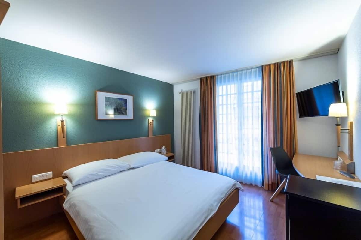 Ein Hotelzimmer mit Bett, Nachttisch, Lampe, Fernseher und Vorhängen.