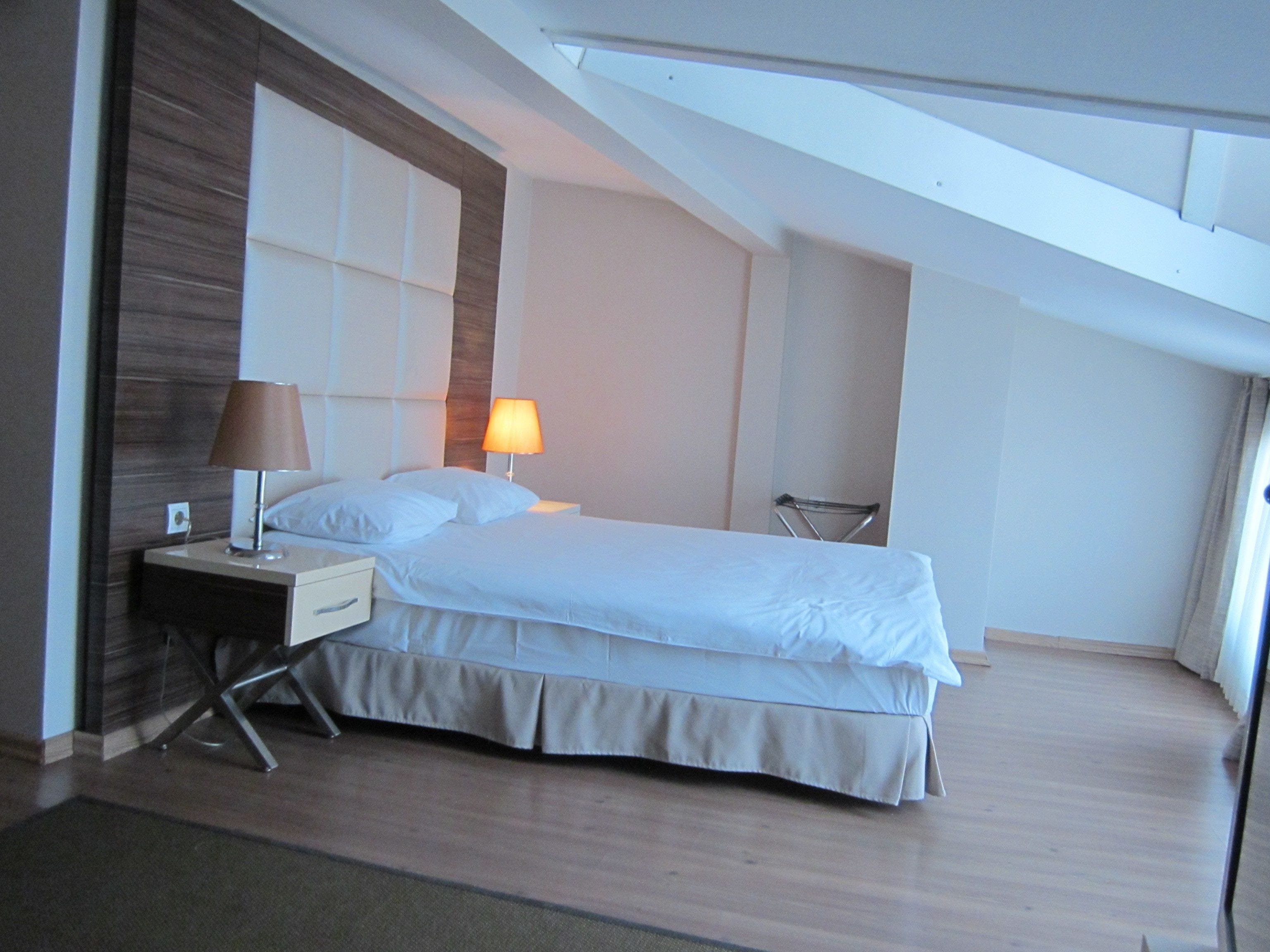 A modern hotel room with a large bed, a bedside table with a lamp, and a chair.