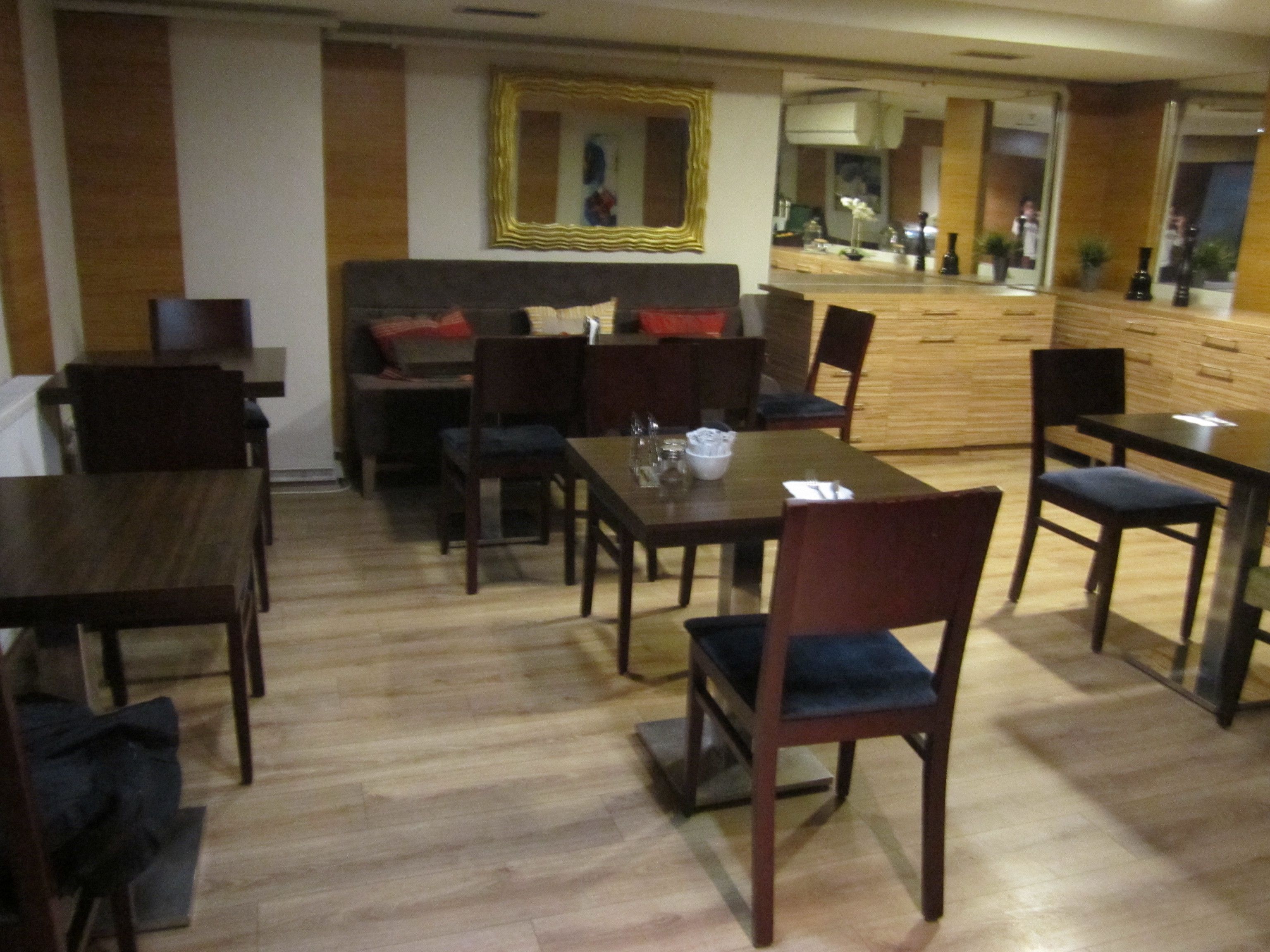 A dining area with wooden tables and chairs, a sofa, and a counter with a mirror.