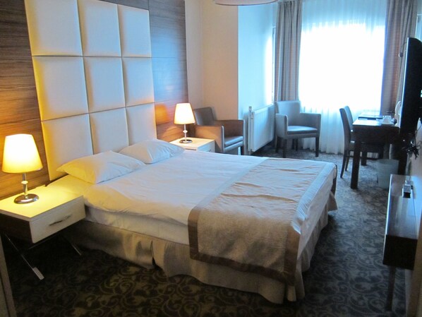 A hotel room with a large bed, two bedside tables with lamps, a chair, a desk, and a television. - Derpa Suite Hotel Osmanbey (Istanbul)
