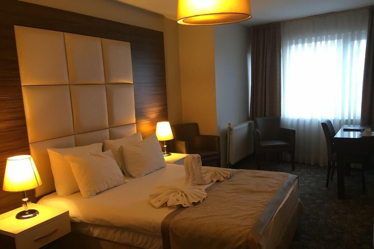 A hotel room with a large bed, two bedside lamps, a desk, and a chair.