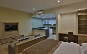 A modern hotel room with a bed, a desk, a TV, and a kitchenette.