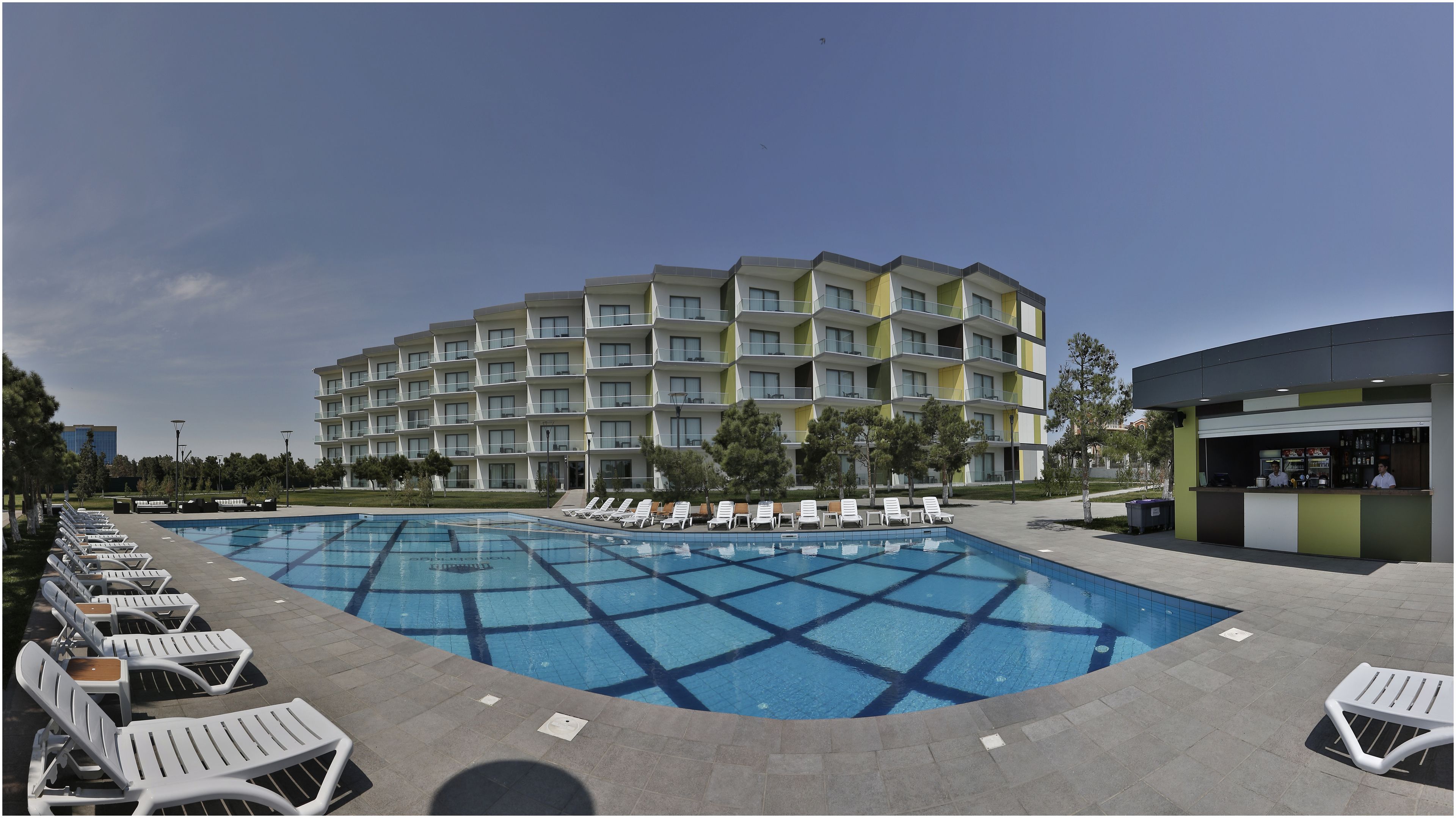 Un hotel con piscina, sillones de descanso y zona de bar.