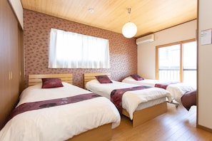 Una habitación con dos camas, piso de madera, un ventanal con cortinas y un equipo de aire acondicionado en la pared.