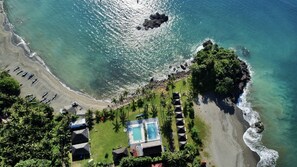 An aerial view of a beach resort with a swimming pool, beach umbrellas, and palm trees. - SAESEA Private Beach & Resort (Cisolok)