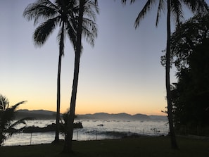 A coastal scene with palm trees, a calm sea, and distant mountains. - SAESEA Private Beach & Resort (Cisolok)