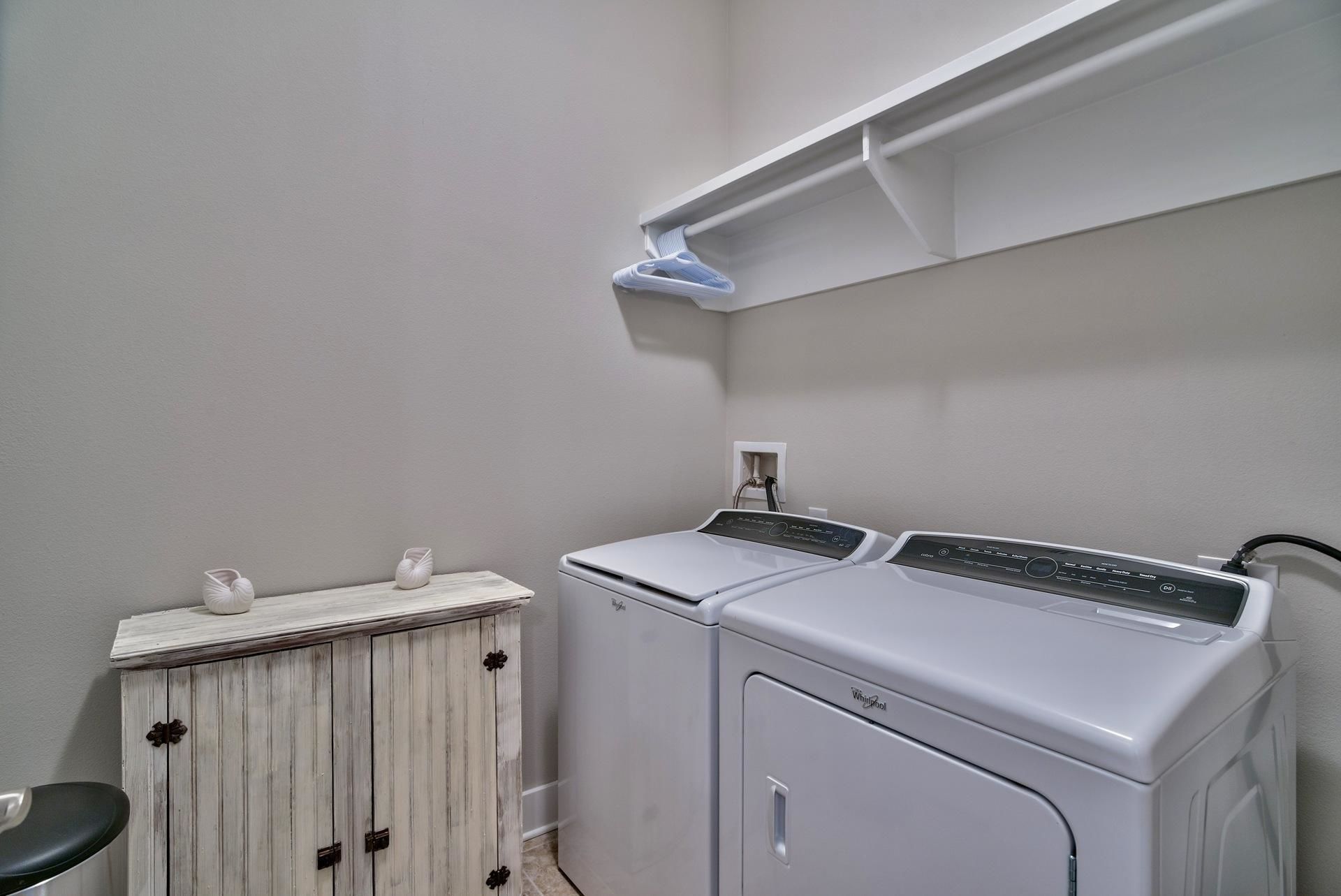 A laundry area with two front-loading washers, a wooden cabinet, and a hanging rack.