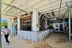 Un espace bar extérieur doté d’une structure vitrée, de chaises blanches et d’un comptoir.