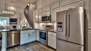 A modern kitchen with stainless steel appliances, a built-in oven, microwave, and refrigerator, a staircase, and a large window providing natural light.