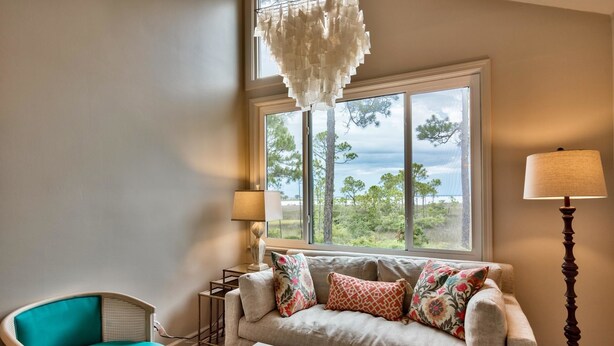 A living room with a sofa, a chair, a lamp, and a view of trees through a large window.