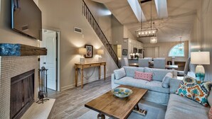 A spacious living room with a fireplace, a staircase, a dining area, and a kitchen.