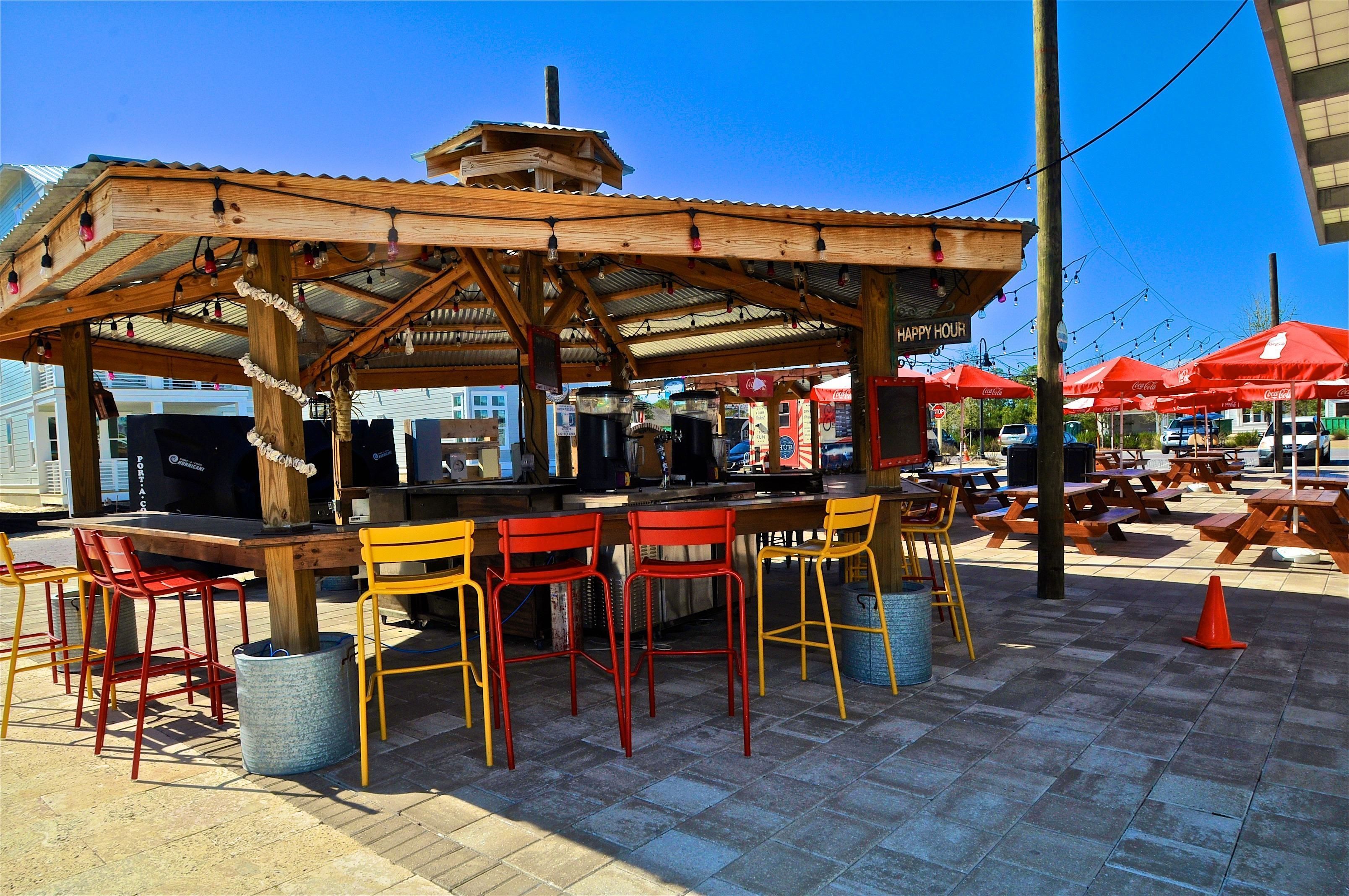 Un área de estar al aire libre con un pérgola de madera, sillas rojas y amarillas, y un paraguas con la marca Coca-Cola.