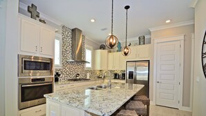 A modern kitchen with stainless steel appliances, a marble island, and wicker bar stools. - Beach Haven 3 Bedroom Condo By Coastal Dreamin (Santa Rosa Beach)